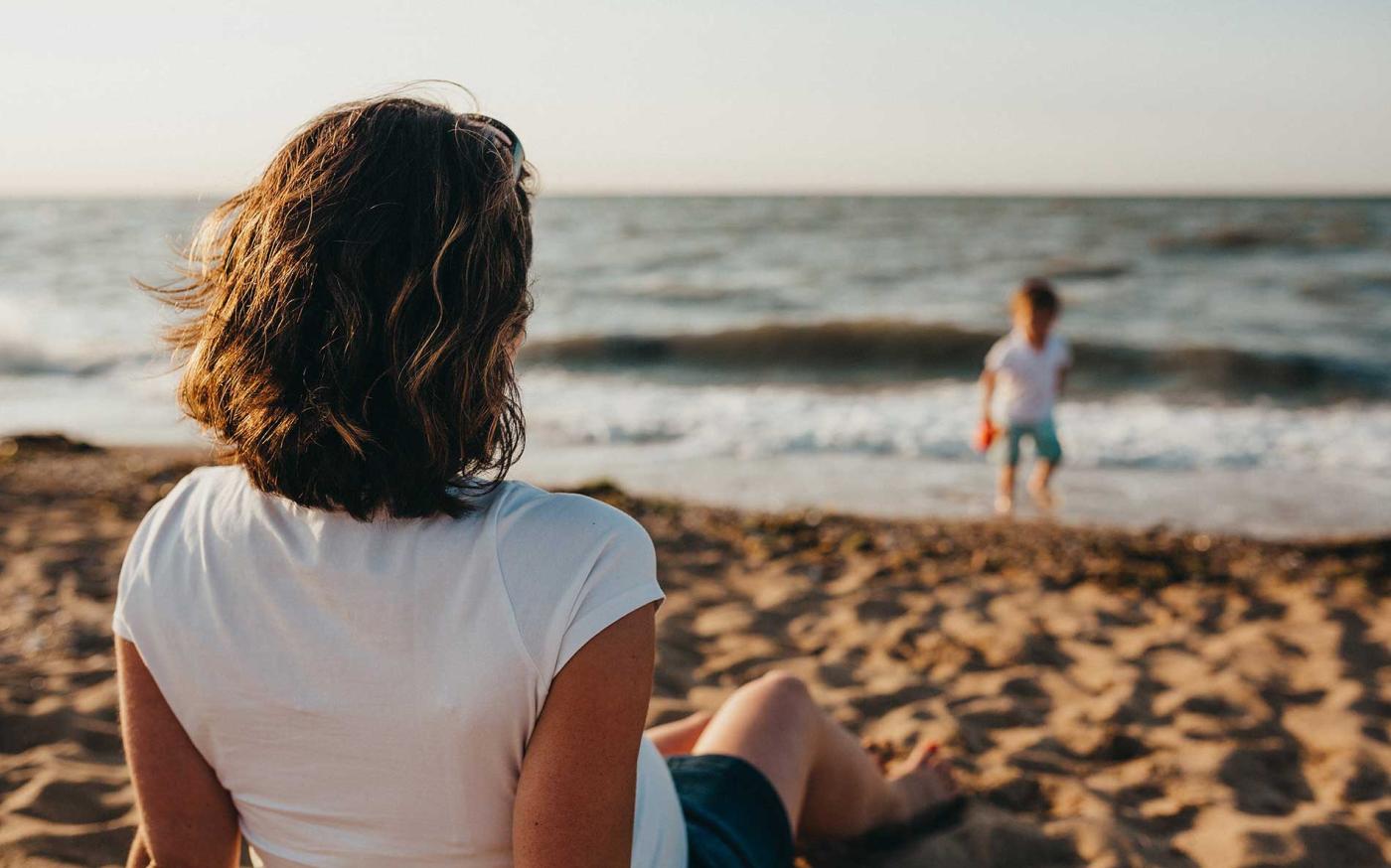 Women on beach staring at child in ocean.